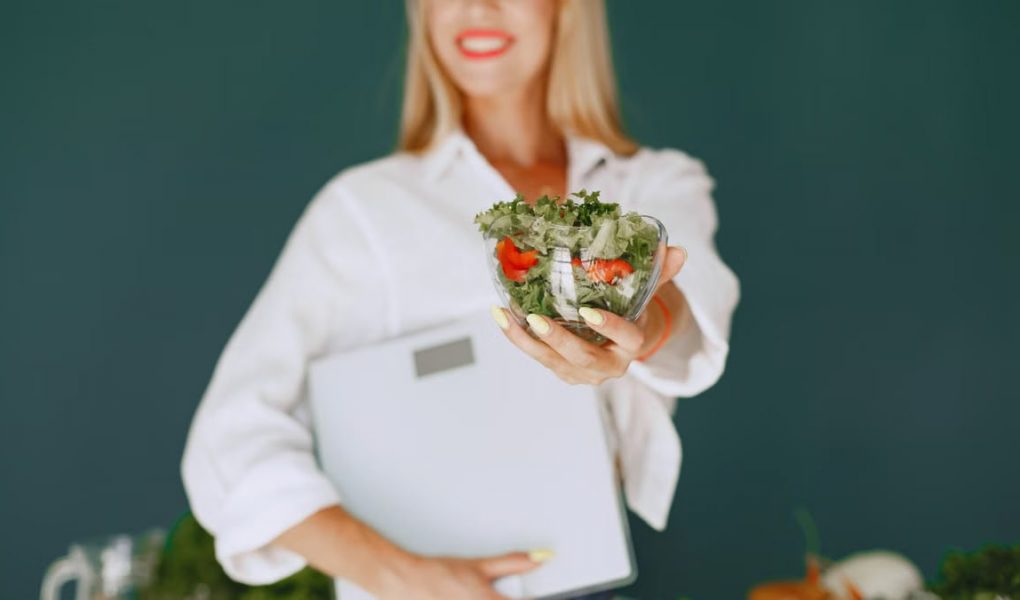 A woman with a vibrant smile offering a fresh salad bowl, promoting healthy eating.