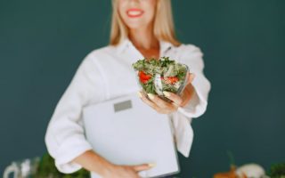 A woman with a vibrant smile offering a fresh salad bowl, promoting healthy eating.