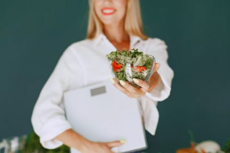 A woman with a vibrant smile offering a fresh salad bowl, promoting healthy eating.