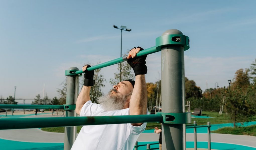 Senior man staying fit with pull-ups in an outdoor park setting, promoting healthy lifestyle.