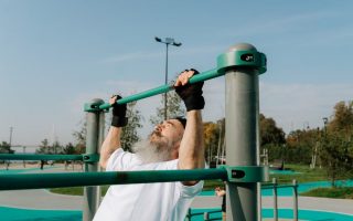 Senior man staying fit with pull-ups in an outdoor park setting, promoting healthy lifestyle.
