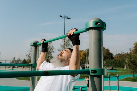 Senior man staying fit with pull-ups in an outdoor park setting, promoting healthy lifestyle.